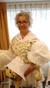 Saines wearing 18th C clothing, with caps on display. 