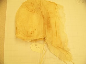 Really badly lit photo of a lappet cap with many stains and tears. 